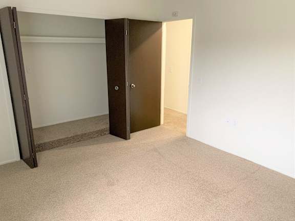 A bedroom with a brown door and a white wall.