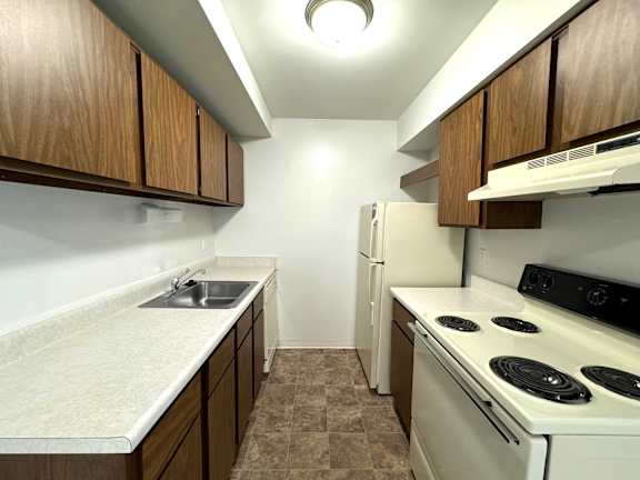 Galley kitchen with white coil stove and wood cabinets at Charter Oaks Apartments, Davison, 48423