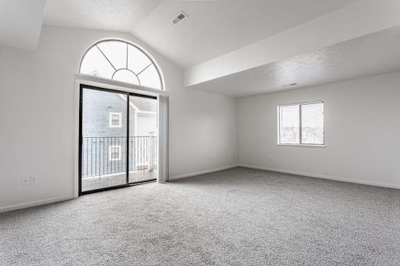 A spacious room with a large arched window and a sliding glass door leading to a balcony