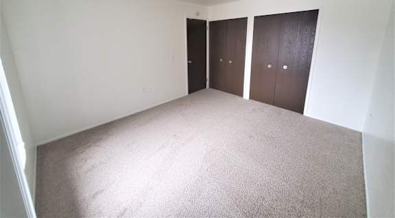 A bedroom with carpeted floor and three brown doors.