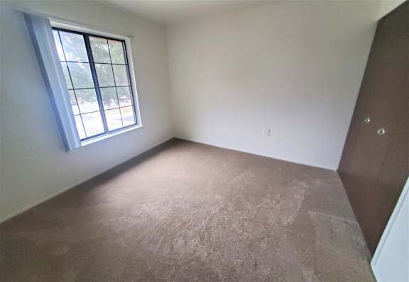 A bedroom with a window and a brown floor.
