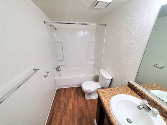 A white toilet sits in a bathroom with wood flooring.