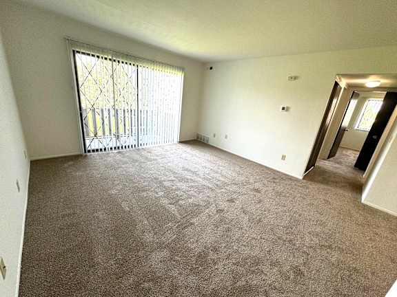 Spacious carpeted living room with sliding patio door at Charter Oaks Apartments, Davison, 48423
