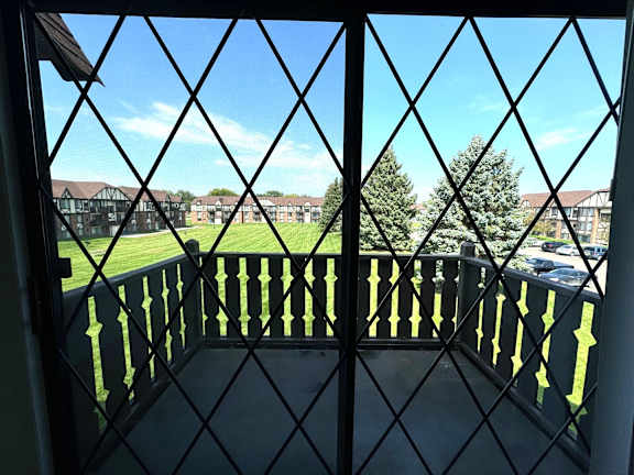 View through diamond lattice window onto green lawn at Charter Oaks Apartments, Davison, 48423