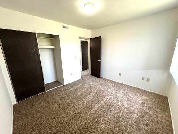 Empty carpeted bedroom with open closet and dark door at Charter Oaks Apartments, Michigan