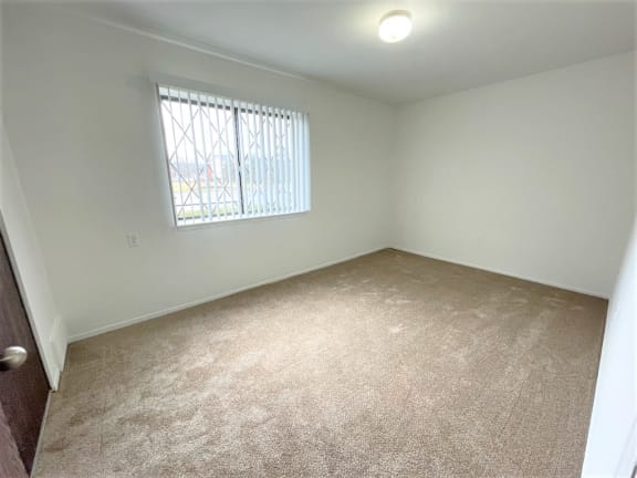 Empty carpeted bedroom with window and security bars 2 at Charter Oaks Apartments, Davison, MI, 48423