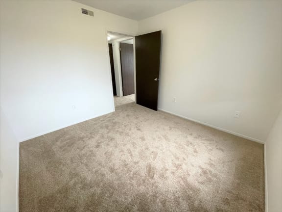 Empty carpeted bedroom with open door and hallway view at Charter Oaks Apartments, Davison, MI, 48423