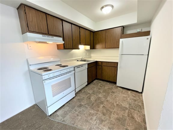 Compact kitchen with white appliances and wood cabinets at Charter Oaks Apartments, Davison