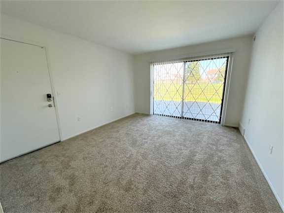 Empty carpeted room with large window and vertical blinds at Charter Oaks Apartments, Davison, 48423