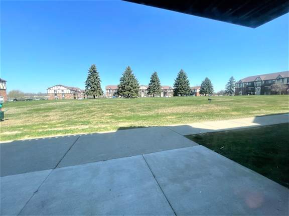 Large grassy common area with evergreen trees and sidewalk at Charter Oaks Apartments, Davison