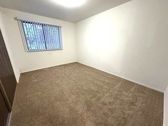 A bedroom with a carpeted floor and a window with blinds.