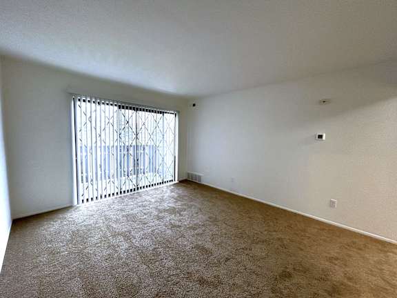 Large empty carpeted room with vertical blinds and security bars at Charter Oaks Apartments, Davison