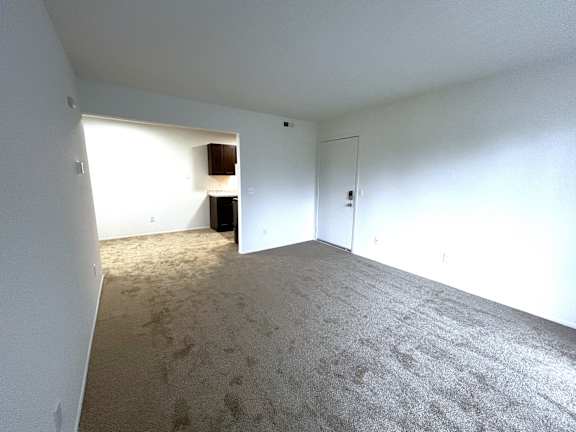 Carpeted living space with adjacent kitchen and entry door at Charter Oaks Apartments, Davison, MI, 48423