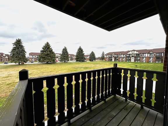 Covered balcony overlooking open green space and pine trees at Charter Oaks Apartments, Davison, 48423