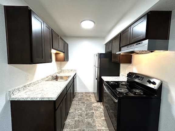 Galley kitchen with granite counters and dark cabinetry at Charter Oaks Apartments, Davison
