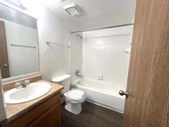 Bathroom with white tub shower combo and wood vanity at Charter Oaks Apartments, Davison