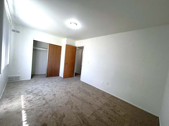 Empty carpeted bedroom with two closets and hallway access at Charter Oaks Apartments, Davison, MI, 48423
