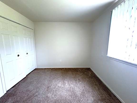 A bedroom with a white door and brown carpet.