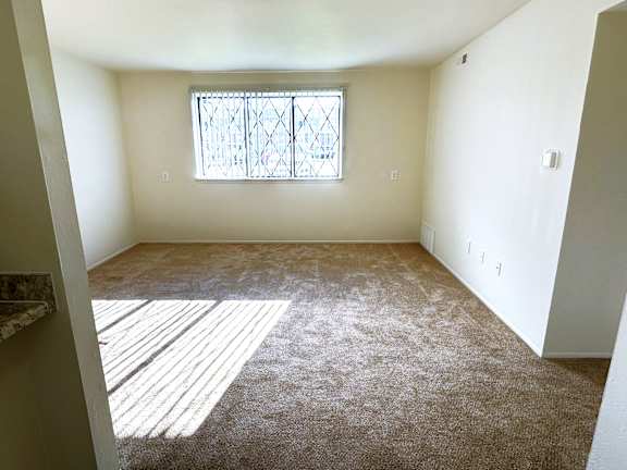 A living room with a carpeted floor and a window with bars.