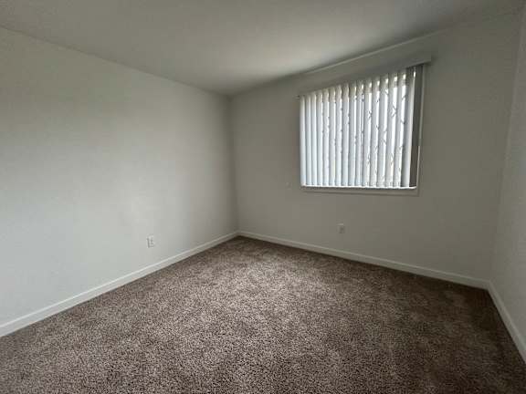 A bedroom with a carpeted floor and a window with blinds.