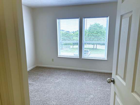 A bedroom with a carpeted floor and two windows.