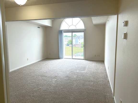 A spacious living room with a carpeted floor and a large arched window.