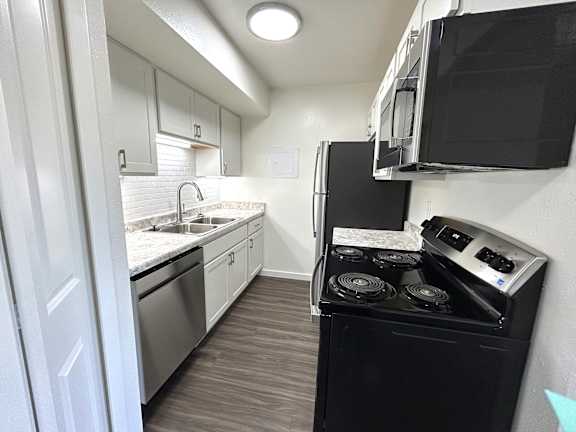 A black stove top oven sits in a kitchen with white cabinets and a black microwave.