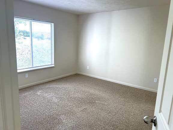 A bedroom with a carpeted floor and a window letting in sunlight.