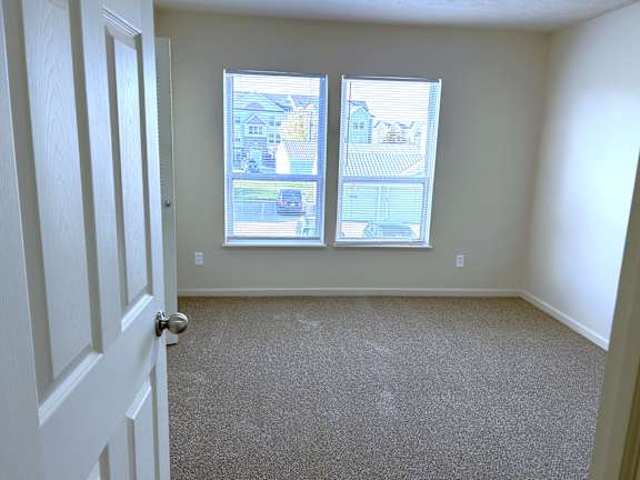 Empty carpeted bedroom with two windows and blinds at Heatherwood Apartments, Michigan