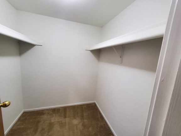 a walk in closet in a white room with a shelf on the wall