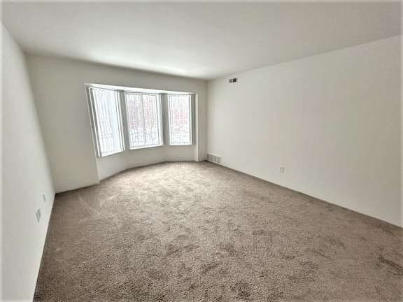 Empty carpeted bedroom with bay window and vertical blinds at Charter Oaks Apartments, Michigan, 48423