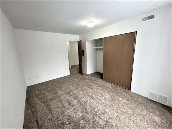 Carpeted bedroom with open closet and hallway door at Charter Oaks Apartments, Davison, MI