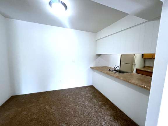 Empty carpeted room with kitchen counter and overhead lighting at Charter Oaks Apartments, Michigan, 48423