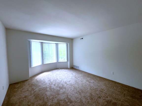 Bright empty carpeted room with three panel windows at Charter Oaks Apartments, Davison, MI