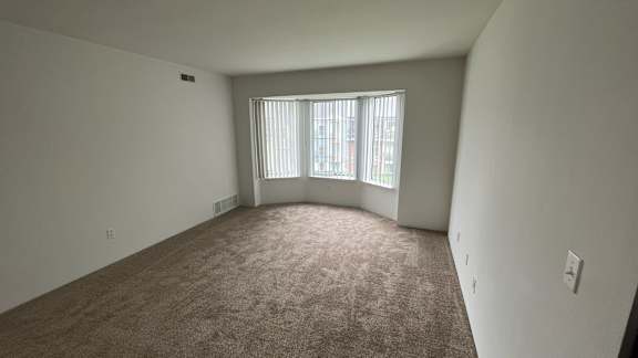 Spacious carpeted living room with bay window and blinds at Charter Oaks Apartments, Davison, Michigan