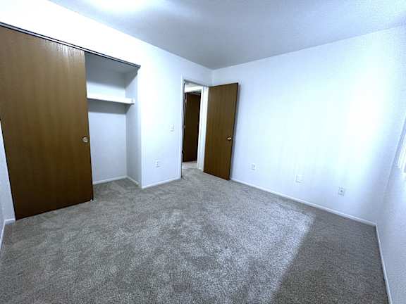 Empty carpeted bedroom with two open wood doors at Charter Oaks Apartments, Michigan