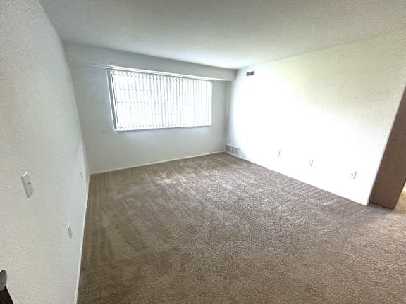Bright carpeted bedroom with vertical blinds and heating vent at Charter Oaks Apartments, Michigan, 48423