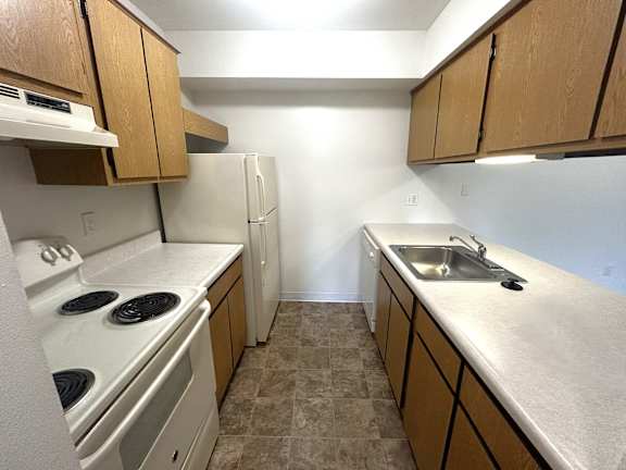 Galley kitchen with white appliances and beige counters at Charter Oaks Apartments, Michigan