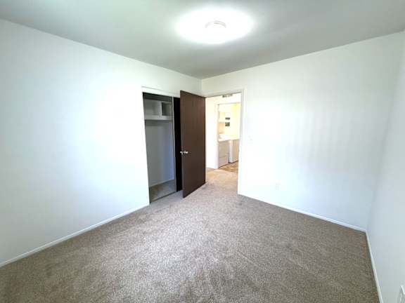 A carpeted bedroom with brown closet doors and a white wall.