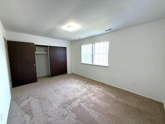 A bedroom with a carpeted floor and a window with blinds.