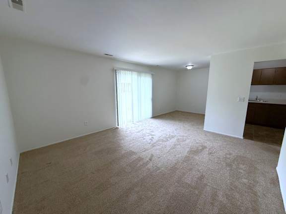 A large living room with a carpeted floor and a window with blinds.