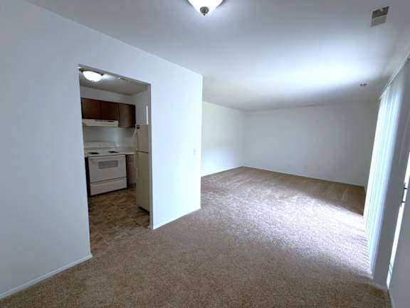 A spacious kitchen with a refrigerator, microwave, and oven is visible through an open doorway.