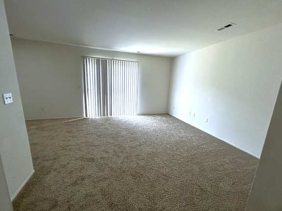 A living room with a carpeted floor and a window with blinds.