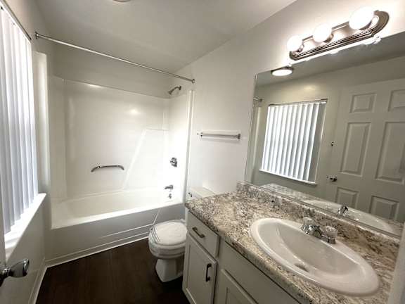 A white bathroom with a marble counter top and a white tub.
