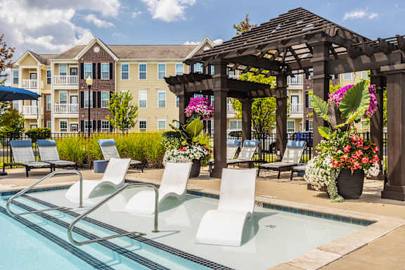 A pool with chairs and a pergola in front of a building.