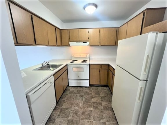 Ushaped kitchen with white appliances and gray tile floor at Charter Oaks Apartments, Davison