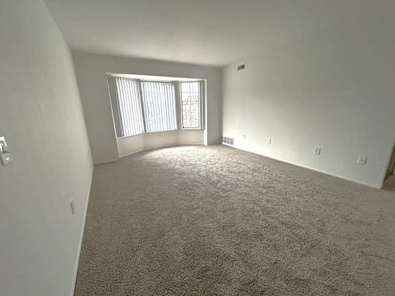 Spacious carpeted living room with vertical blinds 2 at Charter Oaks Apartments, Davison, Michigan