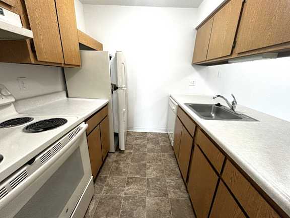 Galley kitchen with white stove and wood cabinetry at Charter Oaks Apartments, Michigan