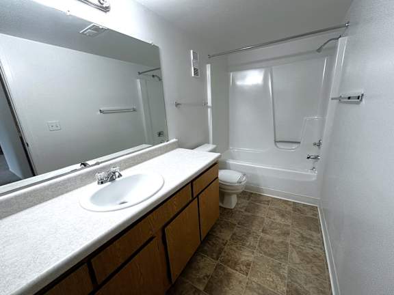 Bathroom with white tub surround and wood vanity at Charter Oaks Apartments, Davison
