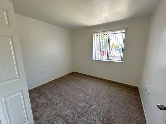 A bedroom with a carpeted floor and a window with blinds.